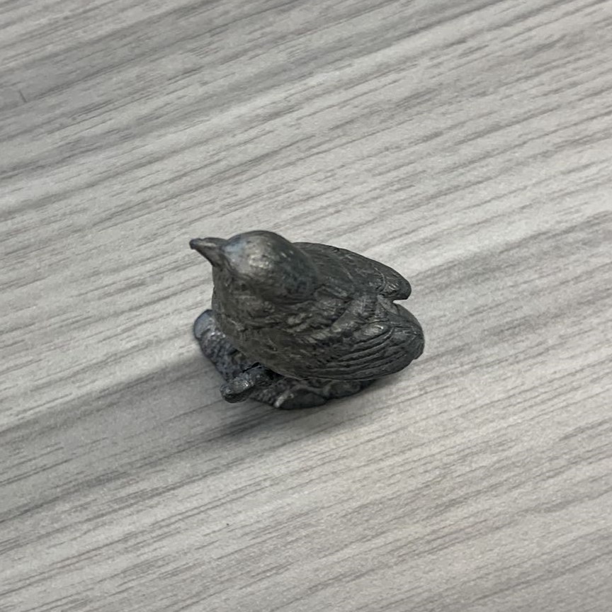 A small bird molded from metal. Smooth and shiny surface with some reflections.