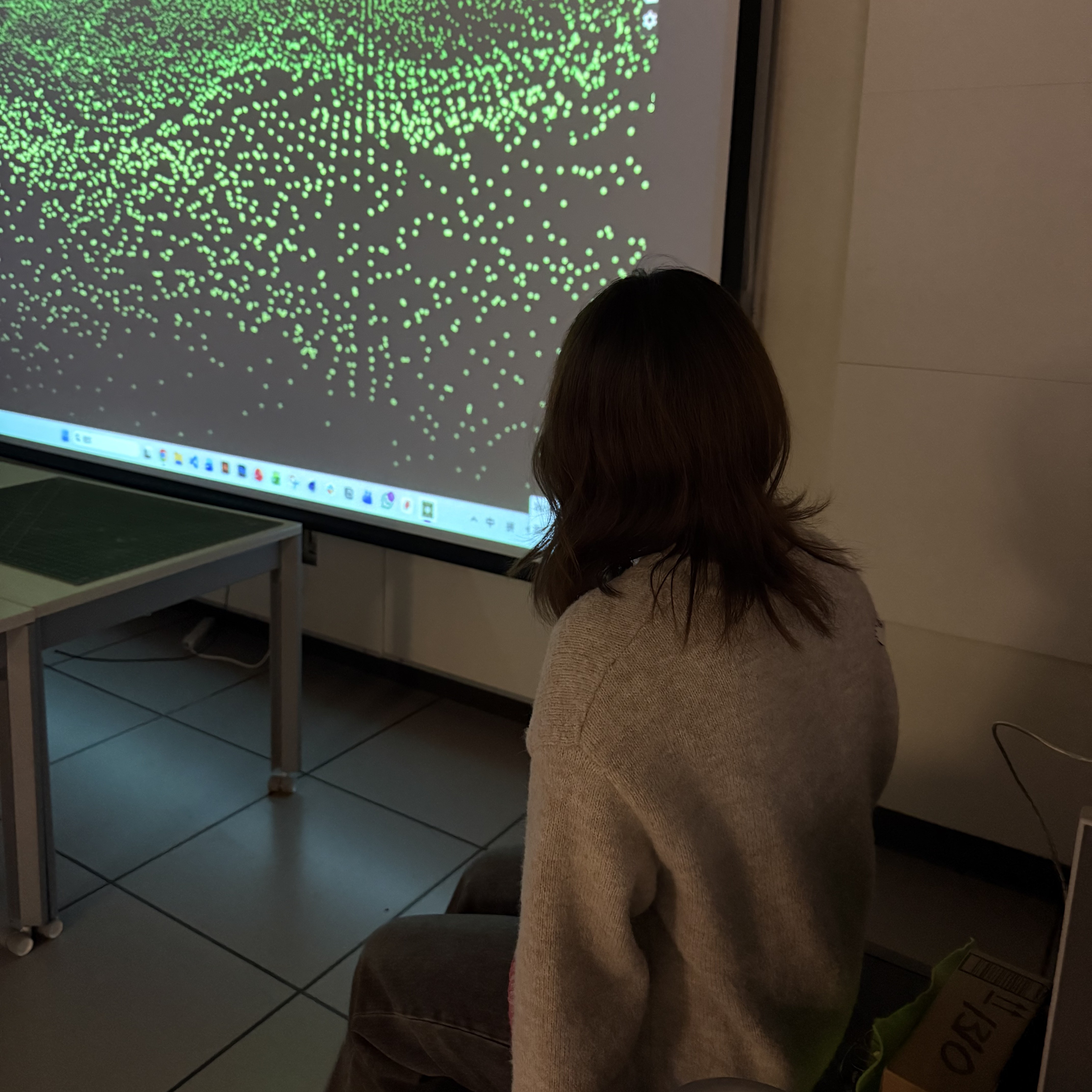 Project 2 continues the direction of Project 1 by exploring how real-time environmental data can shape relaxing visual output. In this stage, we focused on using light-based interaction as the main way to activate and influence the media experience, staying aligned with our goal of creating a device that helps reduce stress.
Our prototype uses a light sensor connected to Arduino to detect changes in brightness. When the environment darkens or when the user leans onto the cushion-like structure, the sensor values shift and trigger TouchDesigner to display soft, calming visuals such as slow-moving particles and gentle gradients. The cardboard cushion houses the circuit and allows the system to activate simply through the user’s presence.
Through this process, we learned how environmental input—especially light changes—can drive responsive media behaviors. By experimenting with particle animations and interactive mapping, we built a foundation for creating soothing sensory experiences. Project 2 becomes an early step toward developing a more immersive and relaxing system in the next stage.
 <a href='https://youtube.com/shorts/X39DAAcwqGI?si=SACyuVqKreyc-OmZ'>Prototype Demo Video</a>